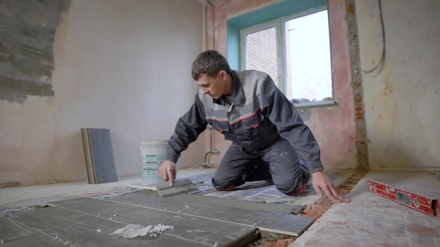 Man working on construction site and laying tiles on floor