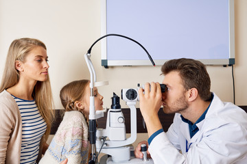 Side view portrait of cute little girl  looking at slit lamp machine during medical check up in eye...