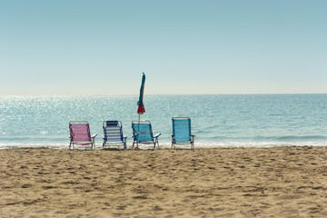 Four colorful hammocks and one closed umbrella in an empty sand beach against the calm sea horizon on sunny day