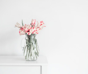 Beautiful bunch of tulips in glass vase on white table at wall. Flowers in interior design. Cozy home. Springtime
