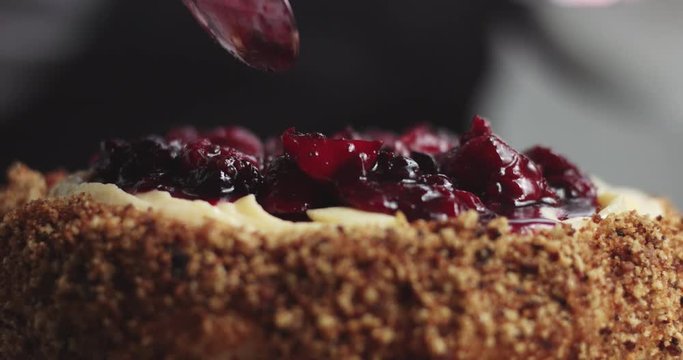Adding forest berries compote to the top of a custard cream sponge cake, close up video