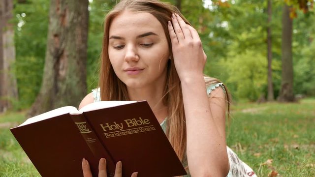 4k. Laying girl  read Bible in park and look at camera. 