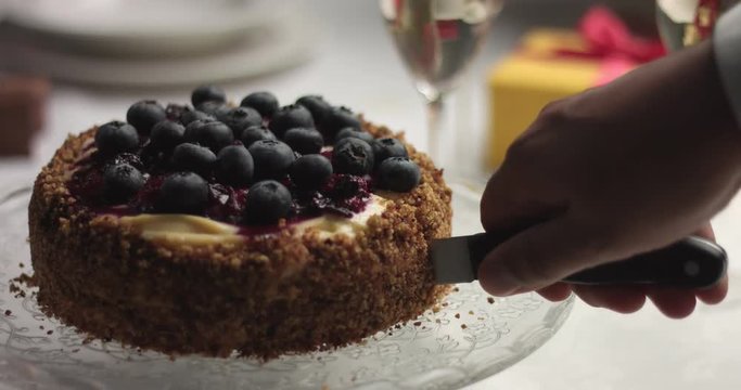 Cutting a homemade birthday holiday cake with custard, forest berry compote and fresh blueberries on a festive table