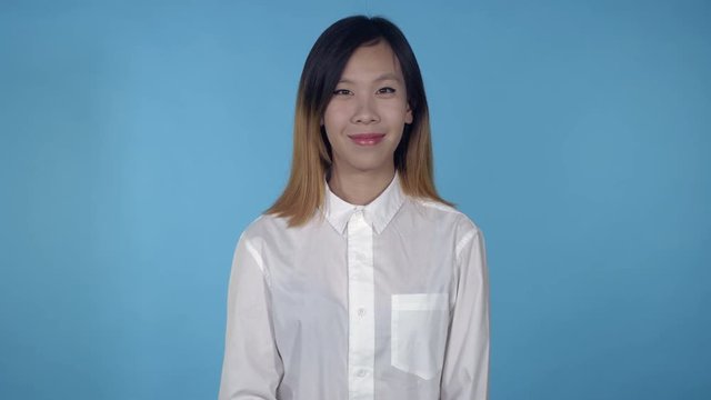 young asian woman posing on blue background in studio. attractive millennial girl wearing white casual shirt looking at the camera smiling