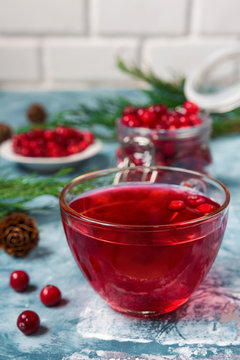 A fresh juicy drink made from cranberry berries in a glass cup on a blue marble background with spruce branches and cones with a copy of the space