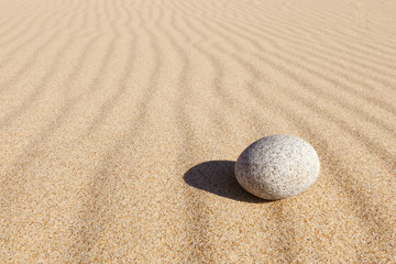 Fototapeta na wymiar White round stone lying on clean sand. Concept of balance, harmony and meditation. Minimalism