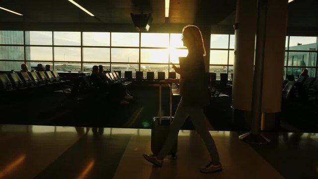 A business woman with a smartphone in her hand and a heap of luggage walks the terminal of the international airport.
