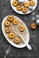 Appetizing ruddy traditional donuts with sugar and cinnamon on an oval dish on a gray grunge trendy background with a Christmas graceful neat decor with silver stars and a garland. Top View.