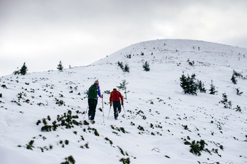 Two friends with backpacks hiking to the top of the mountain in the winter Carpathians mountain