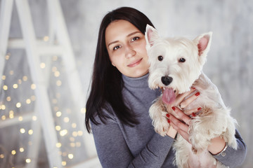 Happy beautiful girl and dog West highland near the Christmas tree. Christmas holiday concept