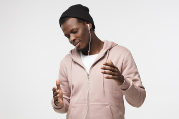 Indoor closeup of young African American male isolated on white background moving his body and hands to sounds of music he is listening to through headphones smiling with pleasure and closed eyes