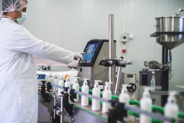 Cosmetics fabric worker typing on fabric production computer while liquid soap going on a production line.