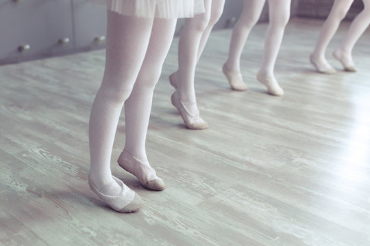 Close up legs in white Czechs of cute little kids dancers on white background. Choreographed dance by a group of small ballerinas practicing at a classical ballet school