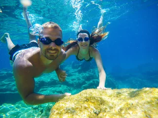 Underwater photo of a young tourist love couple swimming in the turquoise sea under the surface near coral reef while holding hands together for summer vacation.