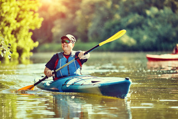  Man paddling a kayak on summer day.