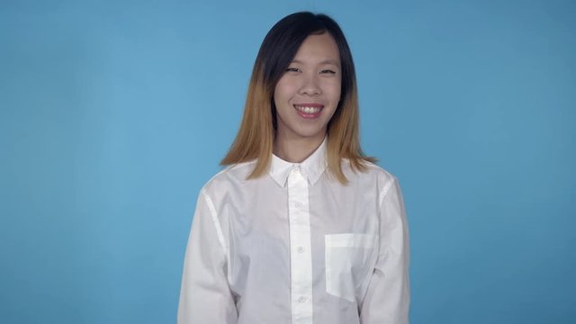 young asian woman posing showing happiness joyful mood on blue background in studio. attractive millennial girl wearing white casual shirt looking at the camera smiling