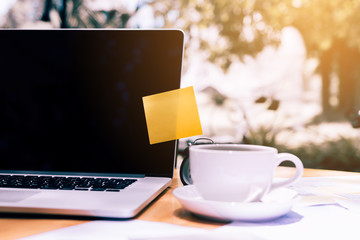 Sticky note pad paste on laptop with coffee cup on wooden desk.