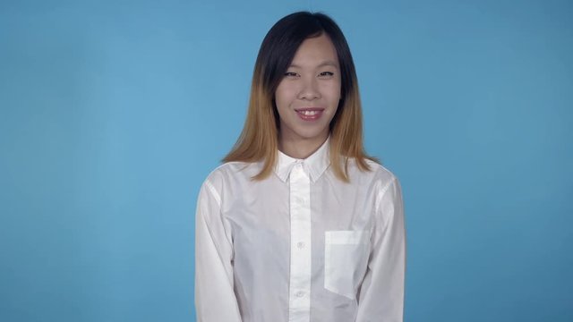 young asian woman posing celebrating victory on blue background in studio. attractive millennial girl wearing white casual shirt looking at the camera smiling