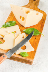 Maasdam radomer cheese on a cutting board, with leaves of basil. On a white stone concrete table. Copy space