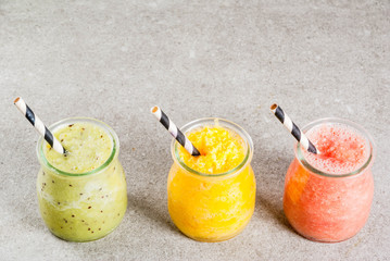Obraz na płótnie Canvas Detox organic diet drinks, homemade tropical smoothies - kiwi, orange, grapefruit, in portioned jars, on a gray stone table. Copy space