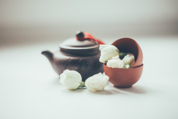 Chinese tea ceremony clay teapot and cups stand on white background next to flowers small white roses