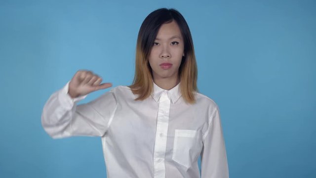 young asian woman posing showing hand gesture like dislike thumbs up and down on blue background in studio. attractive millennial girl wearing white casual shirt looking at the camera