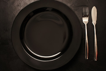 Single plate and cutlery on black background. Sophisticated and simple crockery. Dinner for one and loneliness concept
