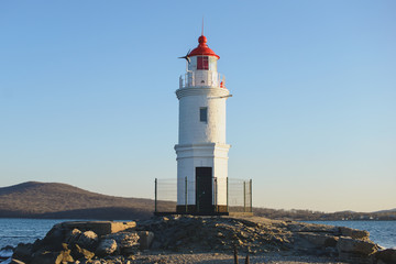 Fototapeta na wymiar Lighthouse on the seacoast at sunset light.