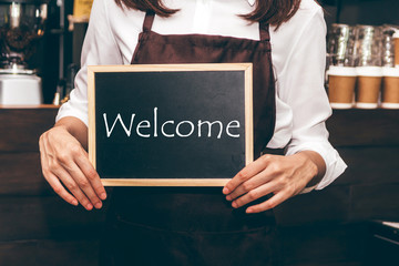Barista holding chalkboard with word WELCOME in coffee shop restaurant