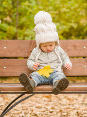 little girl on a bench in an autumn park with a fallen maple leaf