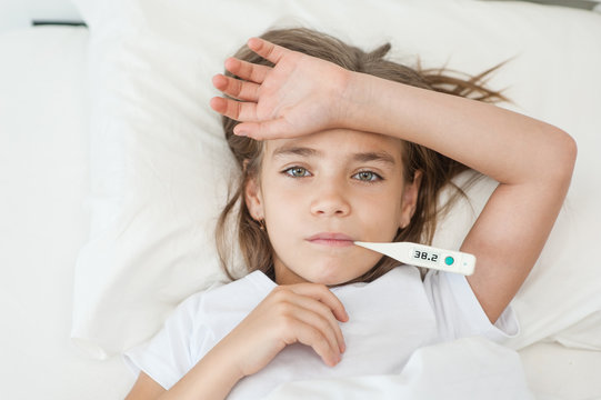 sick girl lying in bed with a thermometer in mouth. Space for text