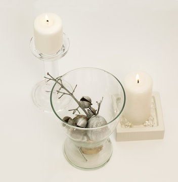 Winter composition – lit, white candle in glass candle-holder and silver decoration in glass vase. White background. 
