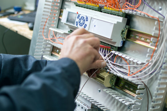 Electrician assembling industrial HVAC control cubicle in workshop. Close-up photo.