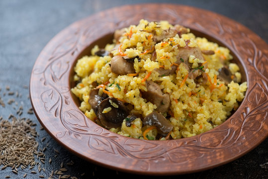 Pilaf with pork meat and mushrooms served in a clay plate, selective focus, shallow depth of field
