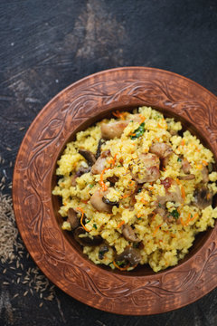 Clay plate with pilaf on a dark brown metal background, view from above, vertical shot