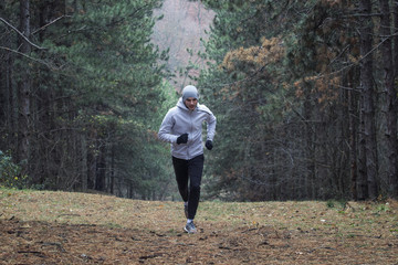 Young sports man running thry forest at cold winter day