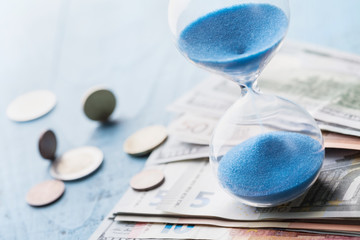 Payment, banking and debt concept. Different money and hourglass on wooden table.