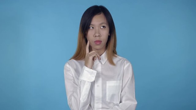 young asian woman posing showing hand gesture find decision on blue background in studio. attractive millennial girl wearing white casual shirt looking at the camera