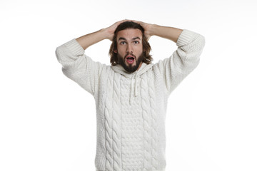 Oh my God, Wow. Cropped studio shot of funny astonished young Caucasian man in hooded knitted sweater holding hands behind his head, staring at camera with eyes pooped out and mouth wide open
