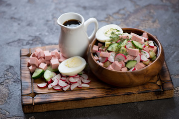 Okroshka or traditional russian cold soup with kvass on a wooden serving tray with some of its cooking components, studio shot