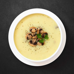 Mushroom cream soup garnished with roasted mushroom slices, black pepper and parsley, photographed overhead on slate with natural light (Selective Focus, Focus on the soup)