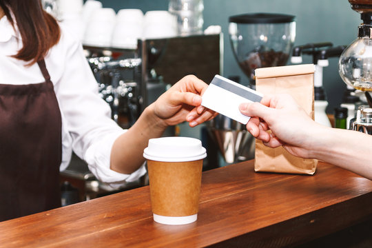 Female Barista  Taking A Credit Card From Customer In Coffee Shop