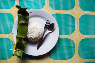 Indonesian dish PEPES IKAN closed in banana leaf - top view with rice and copy space right.