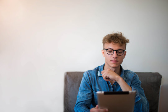 Young Man Successful Publication Specialist Working On Portable Touch Pad, Siting In Office Interior Against Wall With Copy Space. Handsome Male Skilled Proposal Writer Using Modern Digital Tablet