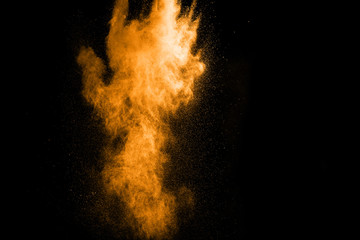 Abstract orange dust explosion on  black background. Abstract gold powder splattered on black...