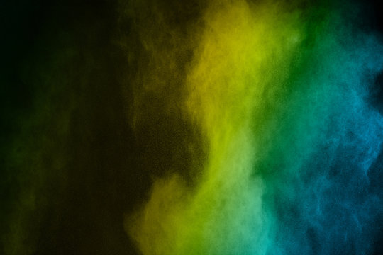 Abstract yellow green and blue powder splatter on black background,Freeze motion of color powder explosion. Splash of color dust on black background.
