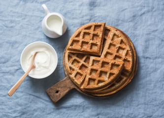 Whole wheat breakfast viennese waffles, cream and milk on blue background, top view