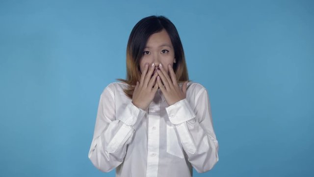 young asian woman posing showing feeling of fear on blue background in studio. attractive millennial girl wearing white casual shirt looking at the camera