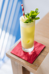 Yellow cocktail with soda bubble topping with mint leaves and slice of lime with red and with strip straw on red napkin.