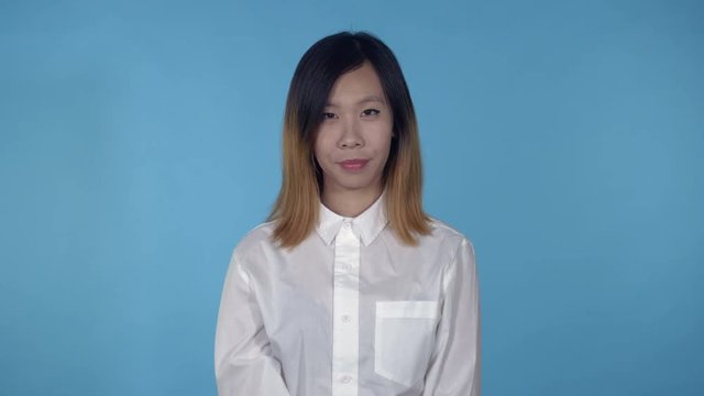 young asian woman tired and overworked on blue background in studio. attractive millennial girl wearing white casual shirt looking at the camera